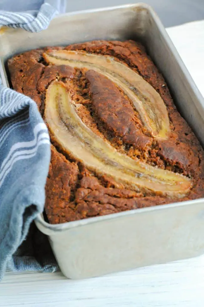 healthier whole wheat banana bread in baking pan with gray cloth with white stripes