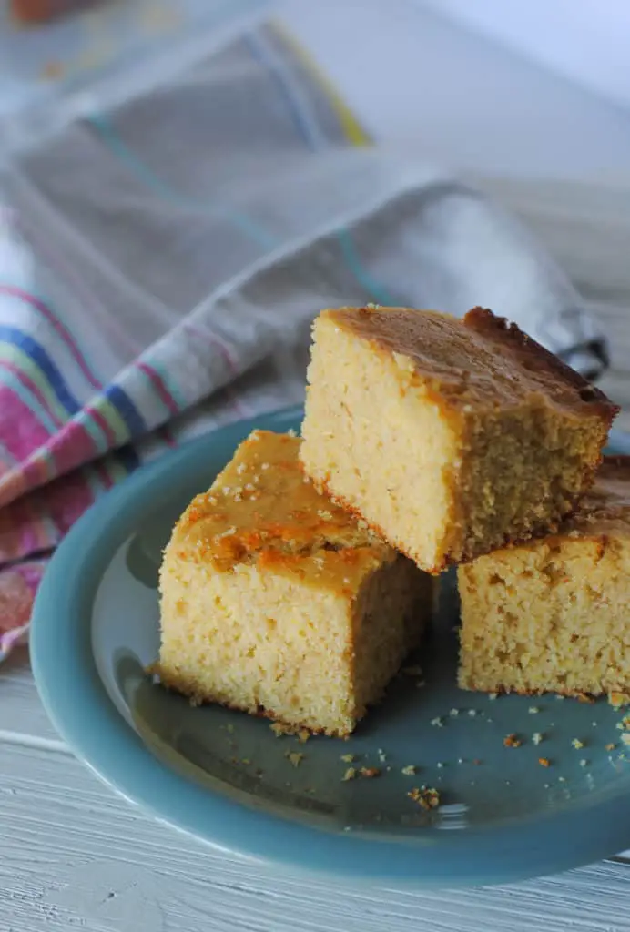 three slices of whole grain cornbread on teal plate with striped linens