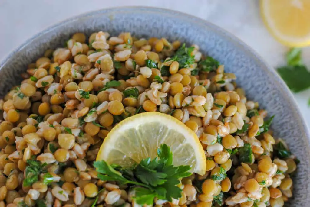 Serving dish with lemony lentil and farro salad garnished with lemon and parsley