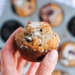 hand holding mixed berry muffin with muffin tin in background