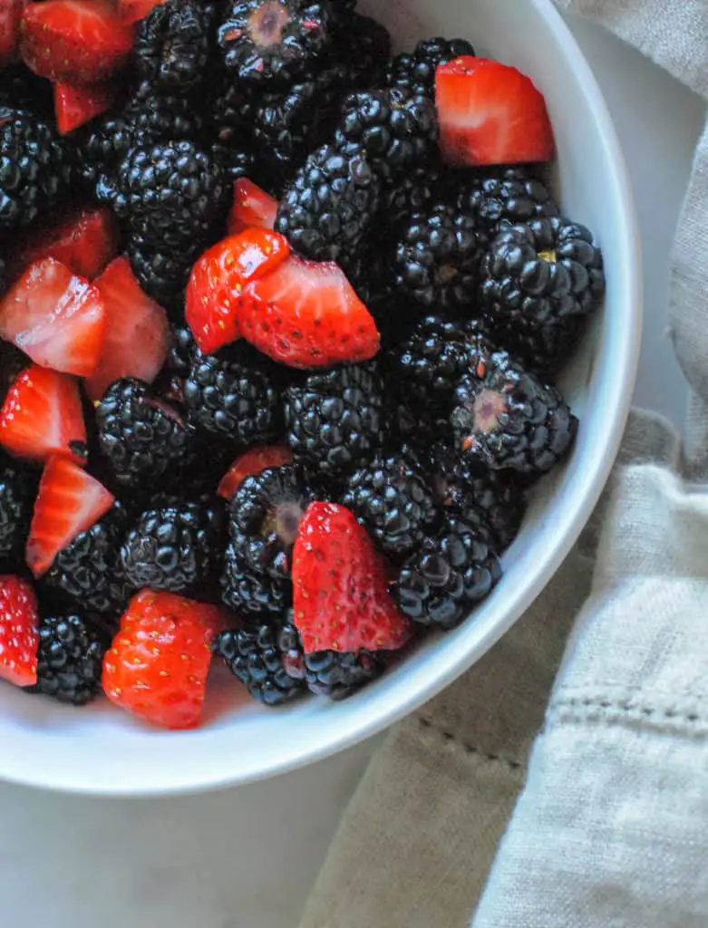 sliced strawberries and blackberries in a white bowl