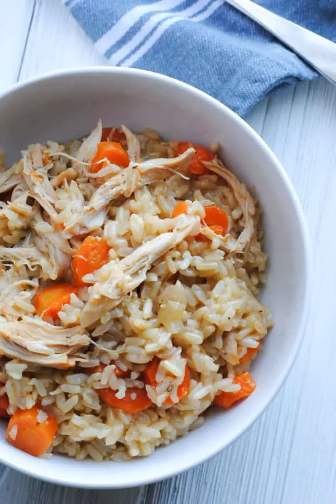 a bowl of chicken and rice with carrots on a white background