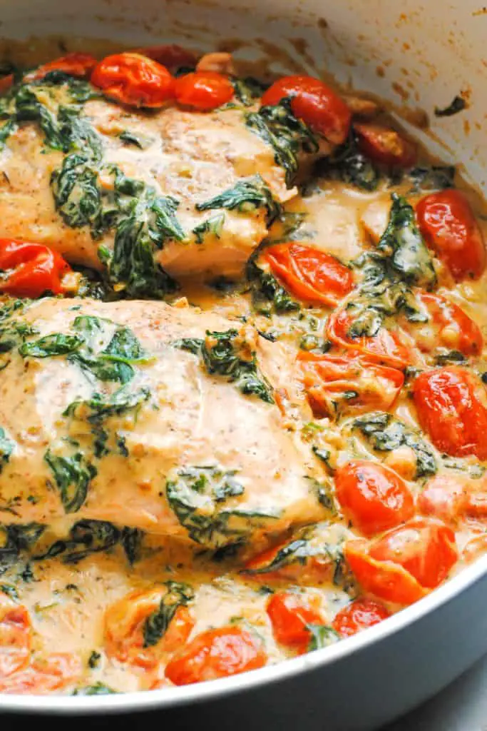 skillet with salmon in a creamy garlic, spinach and tomato sauce