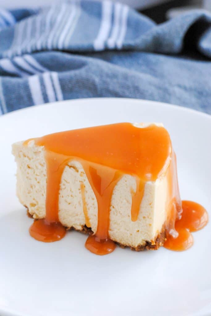 slice of cheesecake with salted caramel sauce drizzled on top set on a white plate with gray background