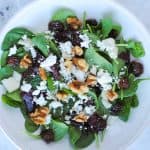 bowl of spinach leaves topped with roasted beets, pears, dried cherries, goat cheese, walnuts